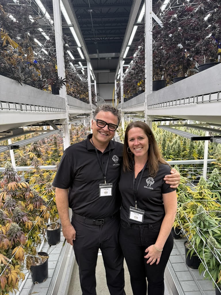 Two smiling adults standing in indoor plant-filled greenhouse facility