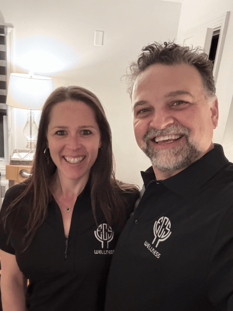 Two smiling adults standing in indoor plant-filled greenhouse facility