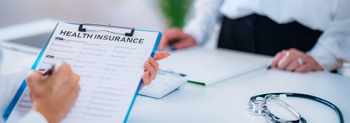 Person filling out a health insurance form at a medical desk.