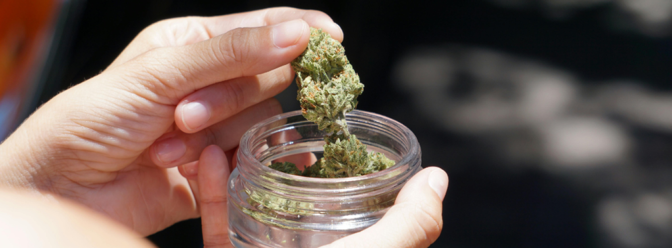 Hands placing cannabis bud into a small glass jar.